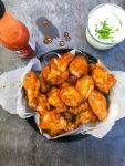 Hot wings with hot sauce and blue cheese on a table.